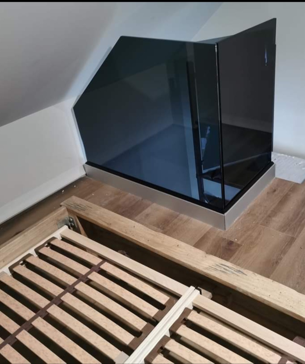 Szklana balustrada zabezpieczająca otwór w podłodze na poddaszu, widok z góry na drewniany stelaż łóżka.