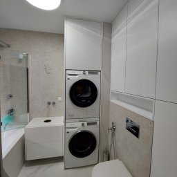 KiKo Concept - Nowoczesna łazienka z zabudową meblową na wymiar w odcieniach bieli i beżu, z pralką i suszarką w słupku oraz wiszącą toaletą.