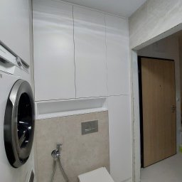 KiKo Concept - Biała zabudowa meblowa w łazience, zintegrowana z pralką i toaletą, na tle beżowych płytek, widoczny również fragment drzwi.