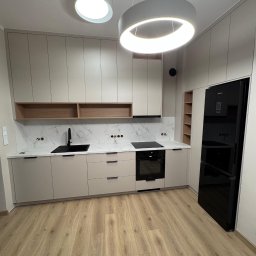 KiKo Concept - Jasna kuchnia z beżowymi szafkami, czarnym zlewem i sprzętem AGD. Marmurowy backsplash i drewniane półki dodają elegancji. Oświetlenie LED podkreśla nowoczesny design.