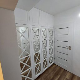 KiKo Concept - Biała szafa wnękowa z lustrami w geometryczne wzory, dopasowana do białych drzwi i drewnianej podłogi, tworząca spójną aranżację wnętrza.