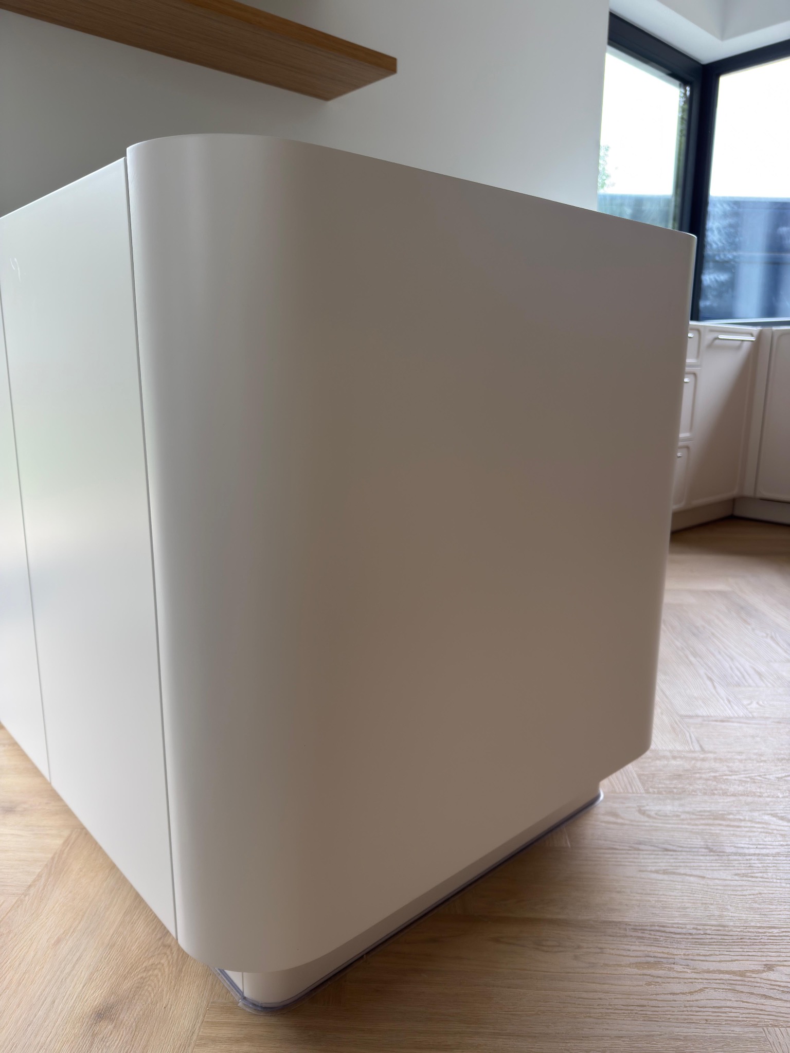 Nowoczesna wyspa kuchenna z zaokrąglonymi krawędziami, w jasnym odcieniu bieli, na tle parkietu w kuchni w Warszawie. Minimalistyczny design.