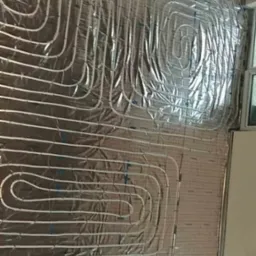 Rury ogrzewania podłogowego ułożone na izolacji termicznej z folii aluminiowej, widoczne niebieskie spinki mocujące rury do siatki.