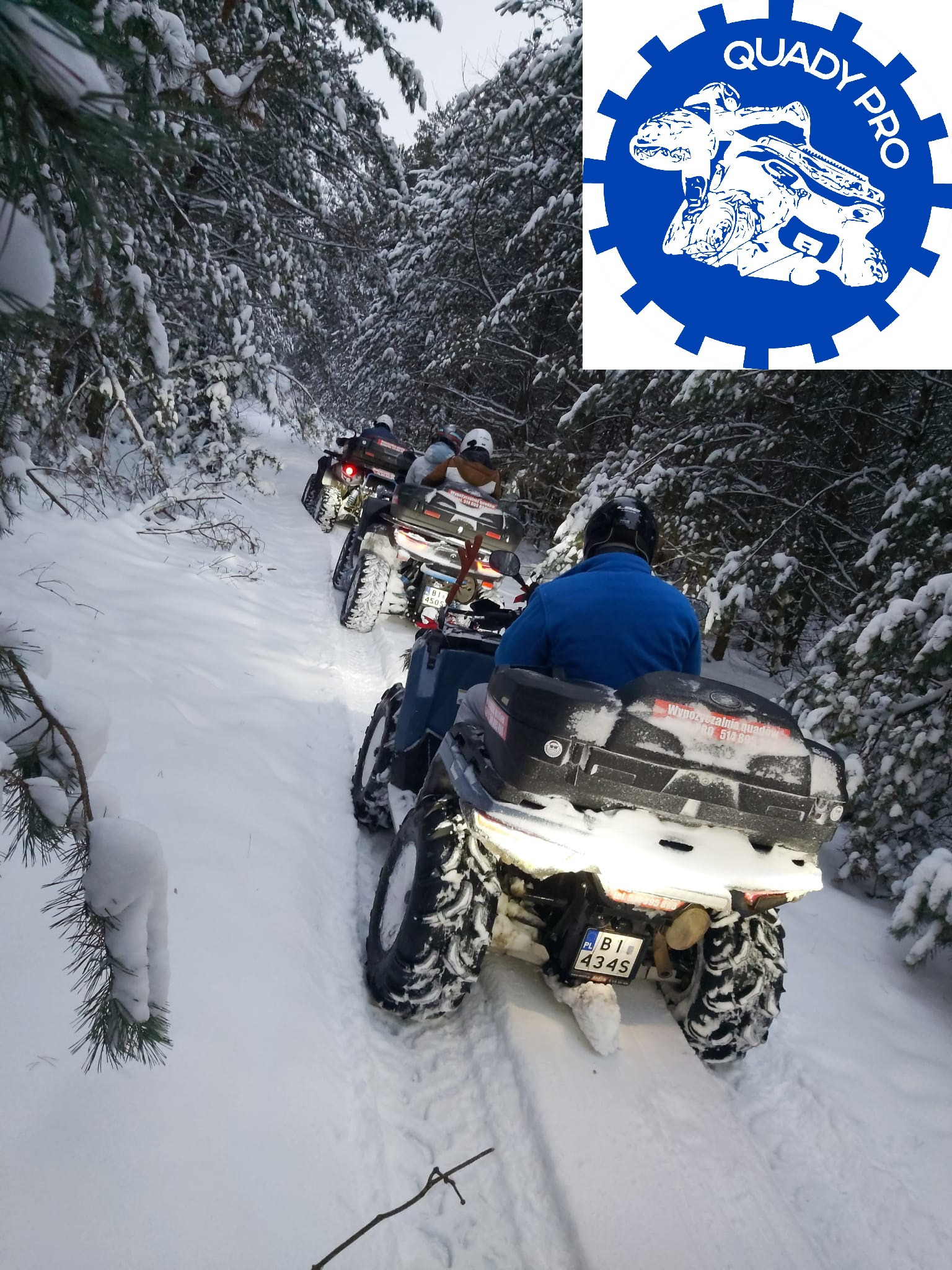 Kolumna czterech quadów poruszających się po ośnieżonej leśnej drodze, widok z tyłu, z logo firmy w prawym górnym rogu.