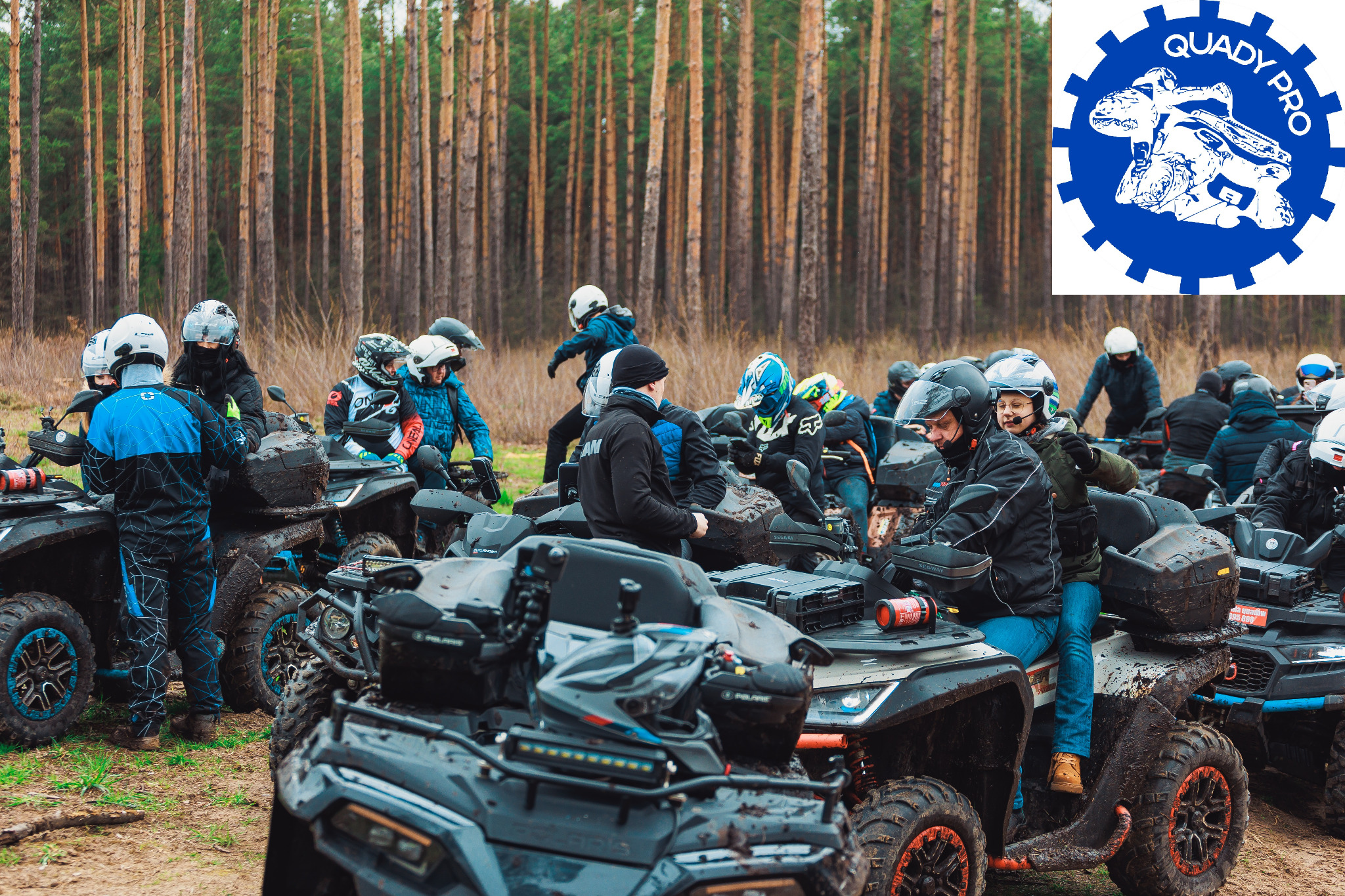 Grupa osób w kaskach siedzi na quadach marki Polaris, ubrudzonych błotem, na tle lasu sosnowego; w prawym górnym rogu logo Quady Pro.
