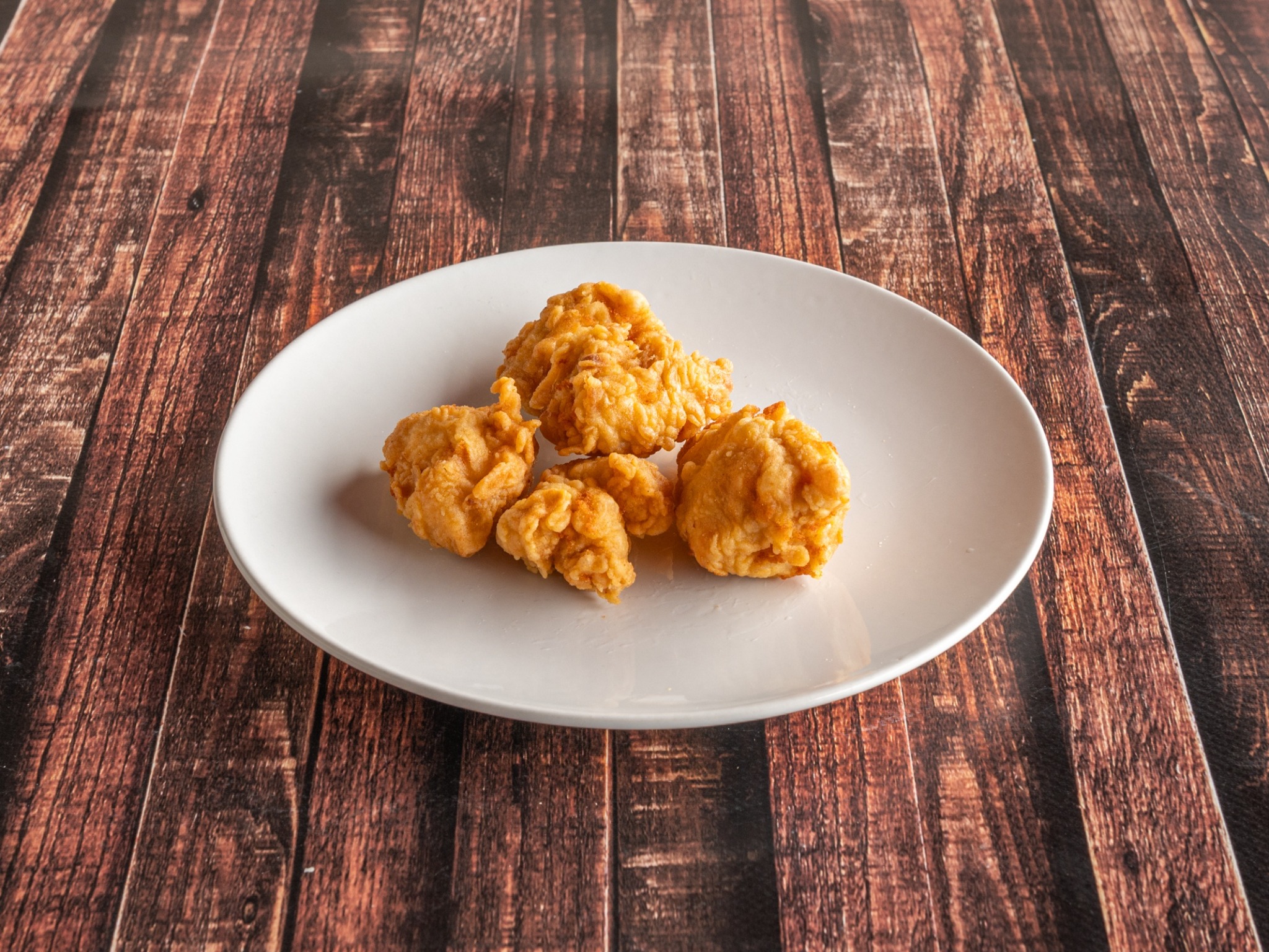 Porcja chrupiących, złocistych nuggetów z kurczaka na białym talerzu, ułożonych na rustykalnym, drewnianym stole.