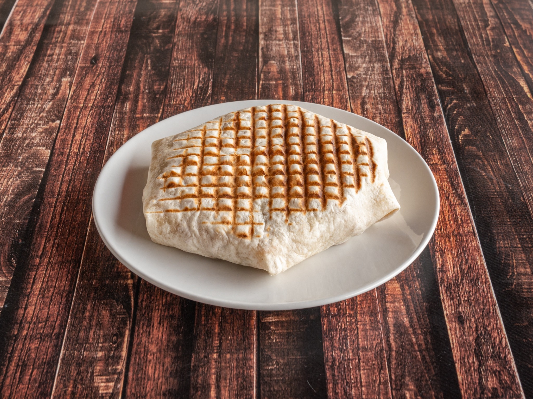 Tortilla wrap z grilla na białym talerzu, ułożona na ciemnym, drewnianym stole.
