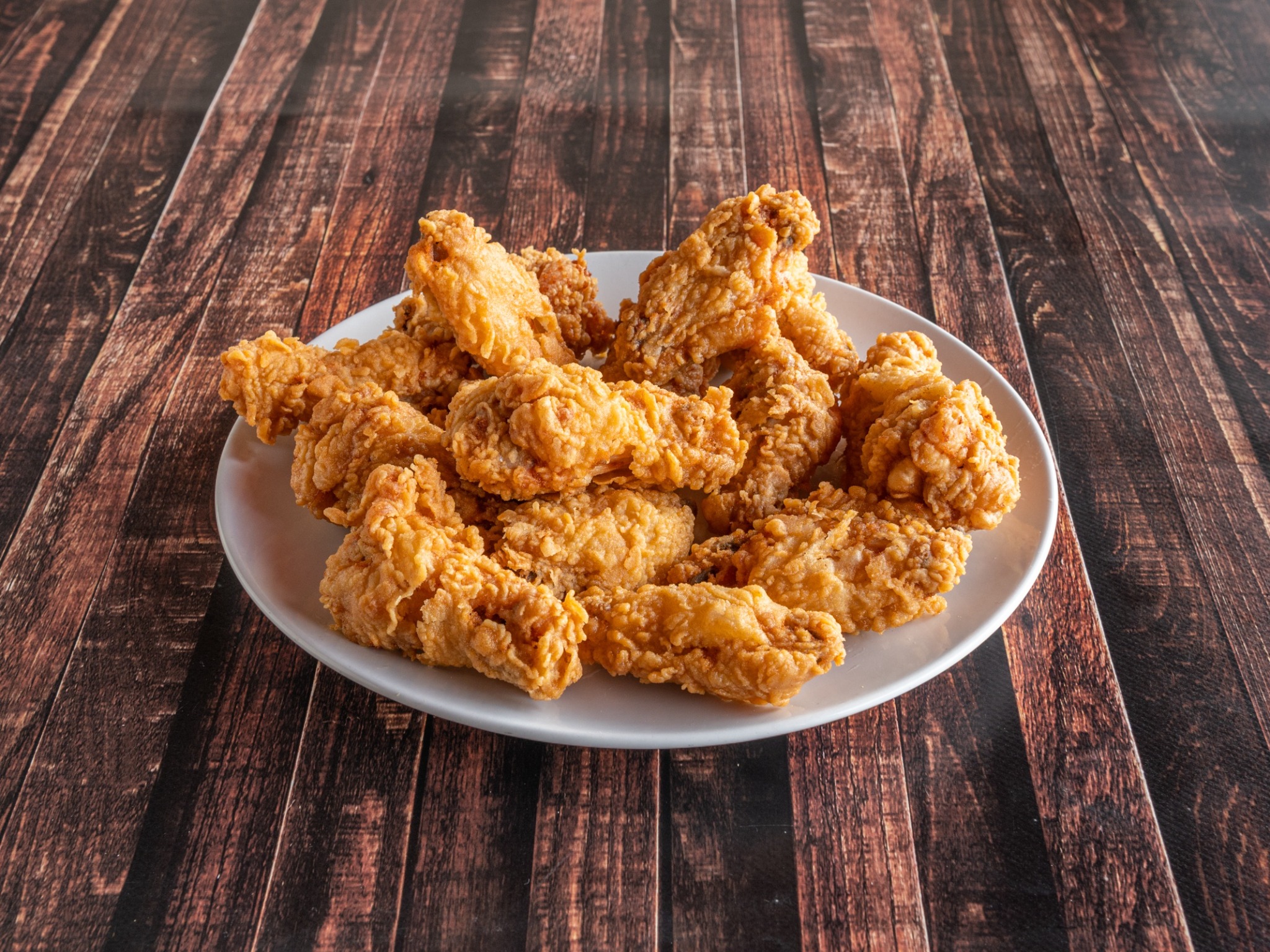 Porcja smażonych udek kurczaka na białym talerzu, ułożona na ciemnym drewnianym stole.