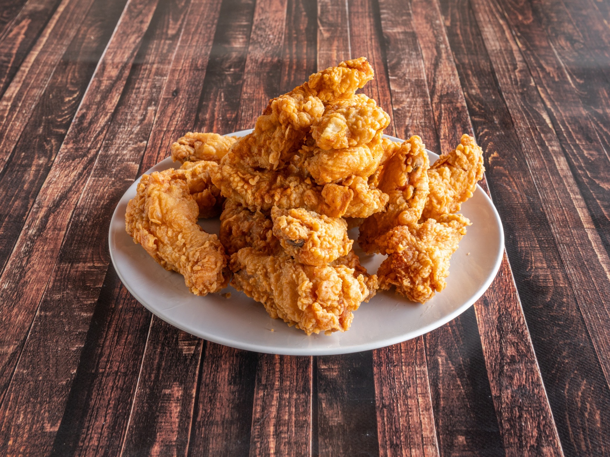 Stos smażonych kurczaków w chrupiącej panierce ułożony na białym talerzu na tle drewnianego stołu.