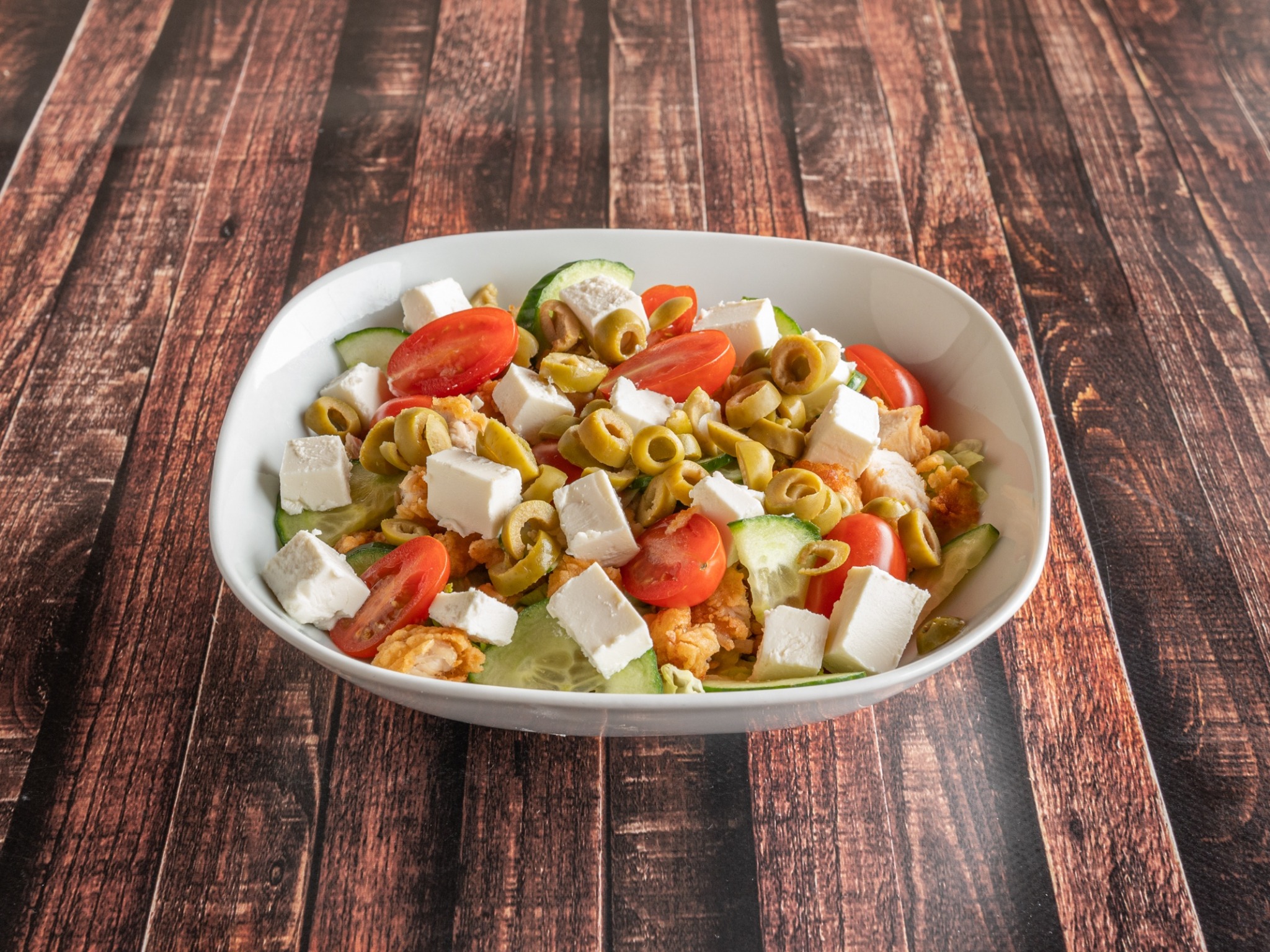 Sałatka grecka z serem feta, pomidorami, ogórkiem i oliwkami w białej misce na drewnianym stole.