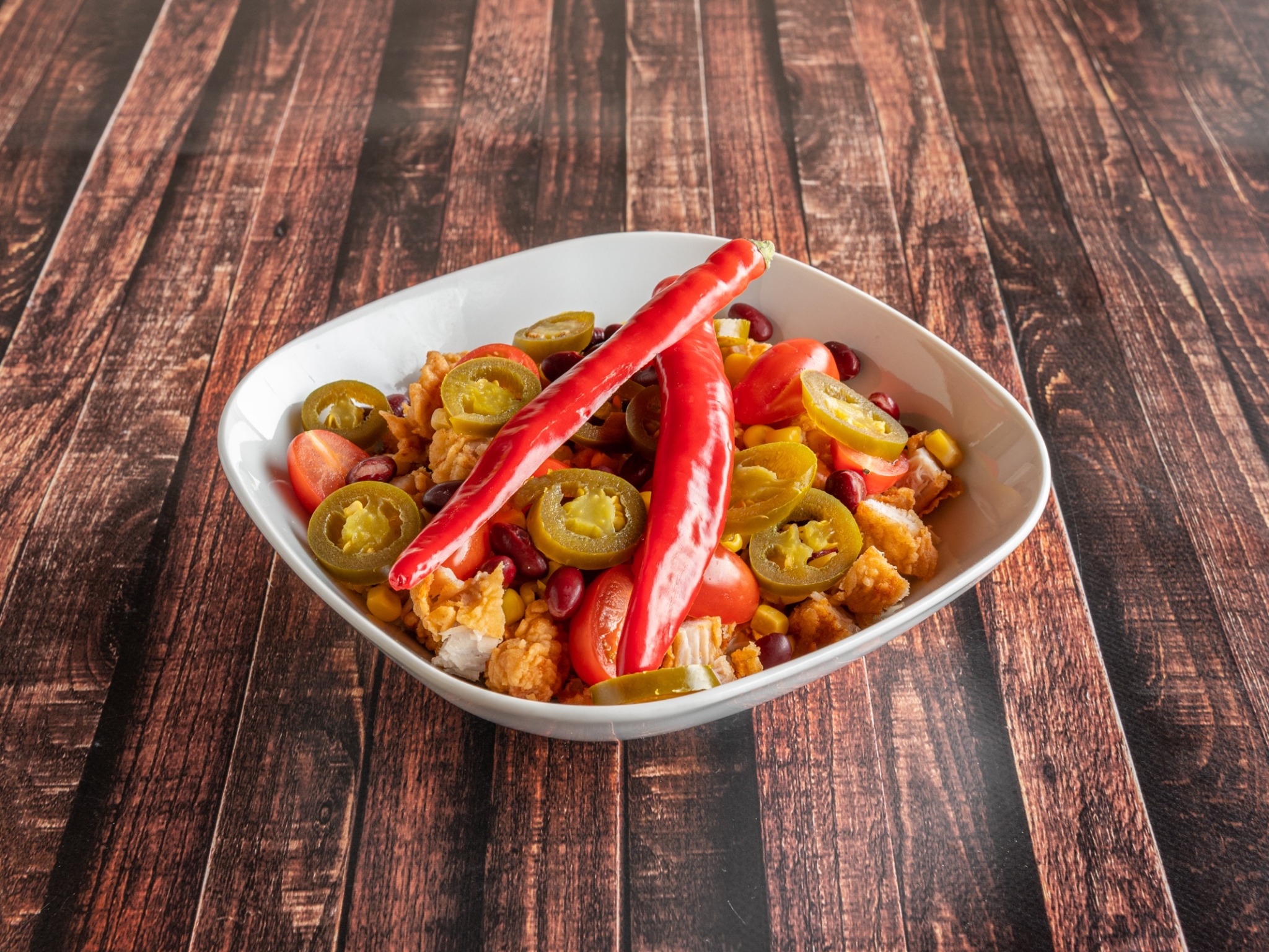 Sałatka z kurczakiem, pomidorami cherry, kukurydzą, czerwoną fasolą i papryczkami jalapeno w białej misce na drewnianym stole.
