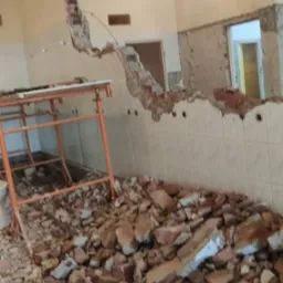 Wnętrze w trakcie rozbiórki w Dąbrowie Górniczej: gruz ceglany na podłodze, fragment zburzonej ściany z widocznymi płytkami i otwory po instalacjach, w tle widoczne kolejne pomieszczenie.