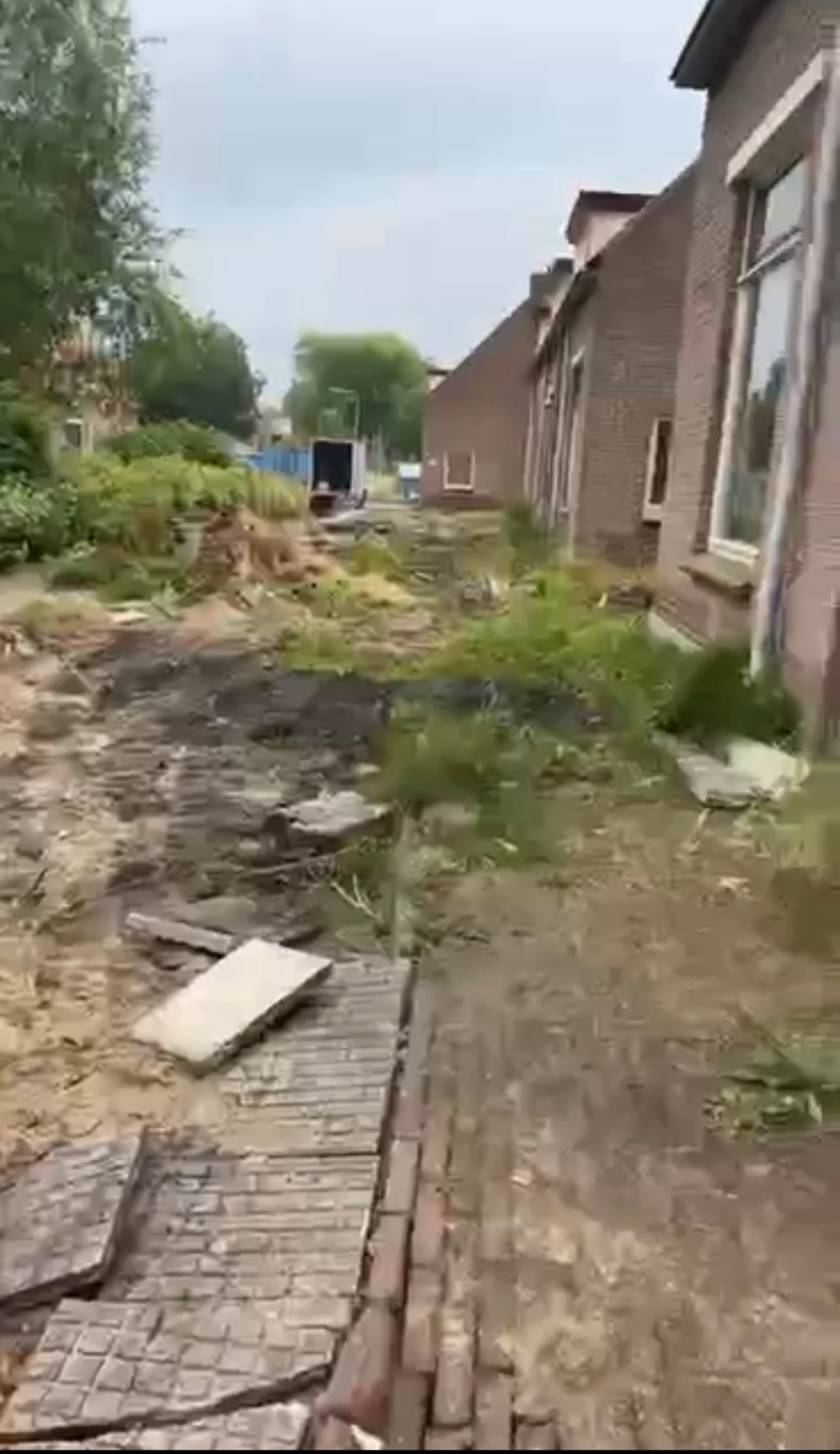 Teren po rozbiórce, z fragmentami gruzu i odsłoniętą ziemią, widoczny budynek z cegły w tle i mała koparka