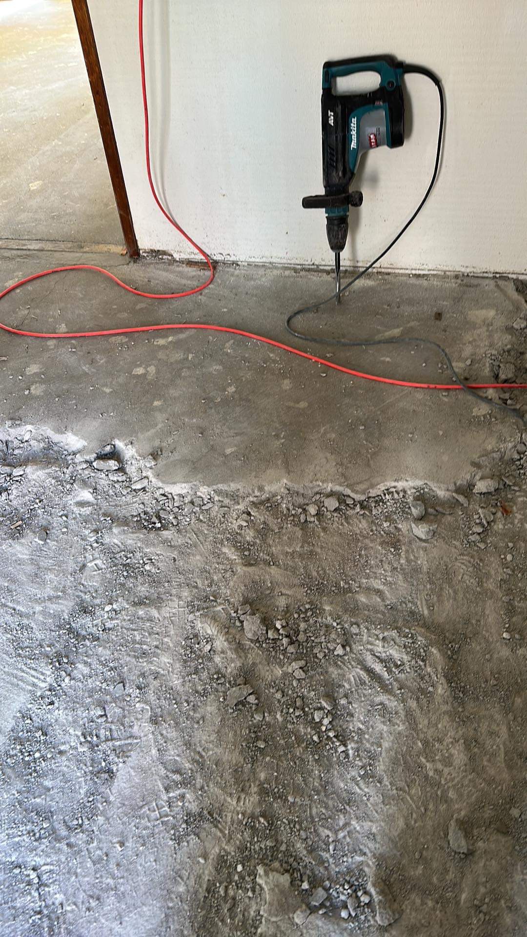 Elektryczny młot udarowy Makita w trakcie wyburzania podłogi betonowej, widoczne okablowanie i gruz.