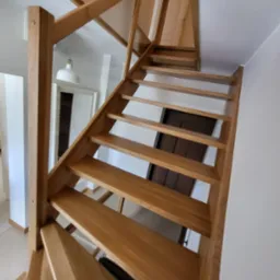 Nowoczesne, drewniane schody z balustradą ze szkła hartowanego, widok od dołu, oświetlenie naturalne i sztuczne, białe ściany w tle.