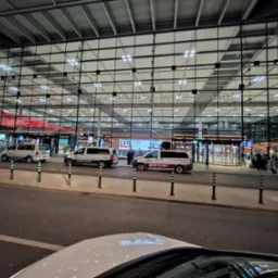Airport Security vans parked in front of Berlin Brandenburg Airport Terminal 1 during evening hours, with reflections on car roof in the foreground.