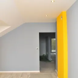 Wnętrze pokoju po malowaniu ścian na szaro i żółto, z widocznymi punktowymi lampami sufitowymi i fragmentem podłogi z paneli.