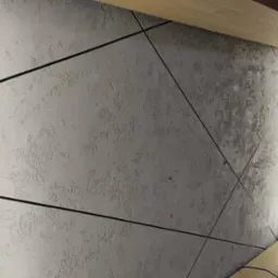 Dekoracyjna ściana z szarego tynku strukturalnego podzielona czarnymi listwami na trójkątne panele, oświetlona pionową listwą LED.