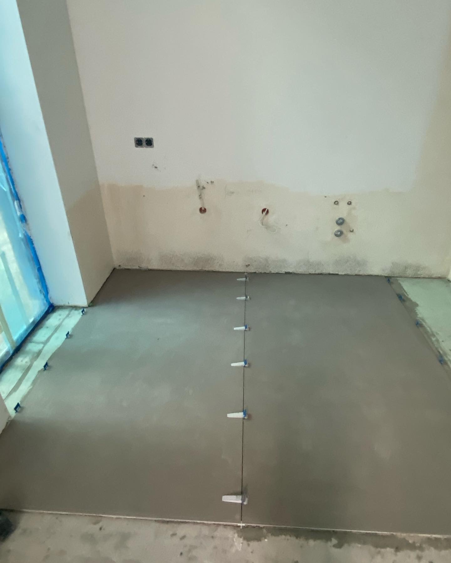 Wylewka samopoziomująca na podłodze z użyciem poziomych krzyżyków dystansowych, przygotowana do dalszych prac wykończeniowych.