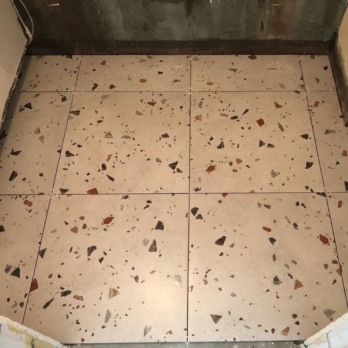 Ułożone płytki podłogowe imitujące lastryko w trakcie fugowania, widoczne krzyżyki dystansowe i surowy stan ścian.