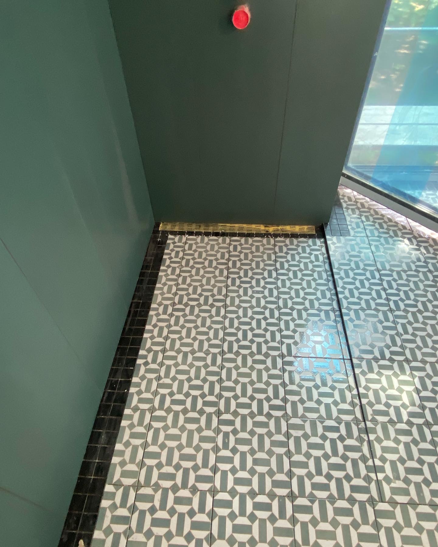 Ułożona podłoga z szaro-białych płytek o geometrycznym wzorze, z czarną obwódką przy ścianie i złotą listwą progową, widok z góry.