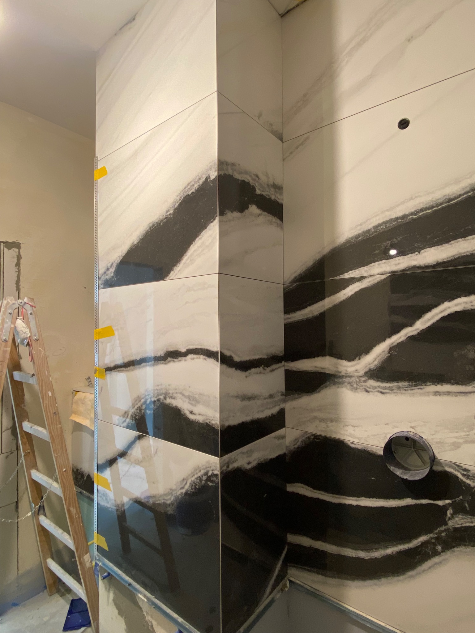 Montaż płytek imitujących marmur w łazience, widoczna drabina i żółte kliny dystansowe.