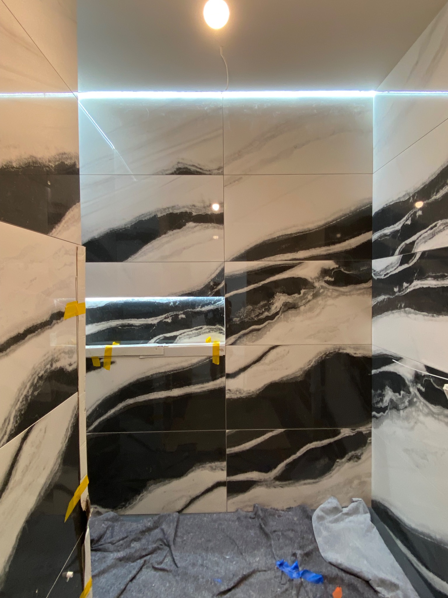 Ściana w trakcie kładzenia płytek imitujących marmur w Markach, z podświetleniem LED i widocznymi taśmami mocującymi.
