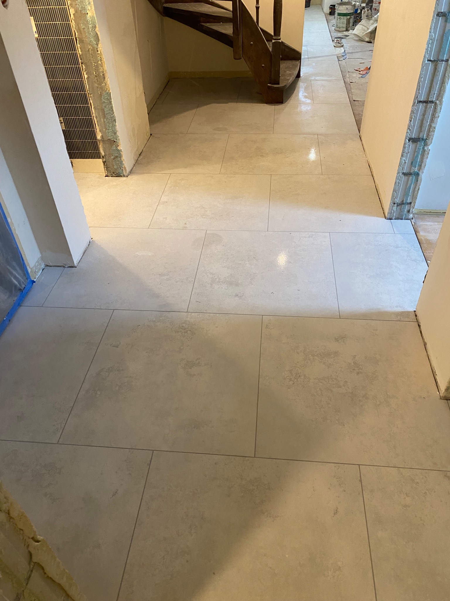 Ułożona jasna, matowa podłoga z płytek w korytarzu podczas remontu, widoczne przygotowane ściany i schody w tle.