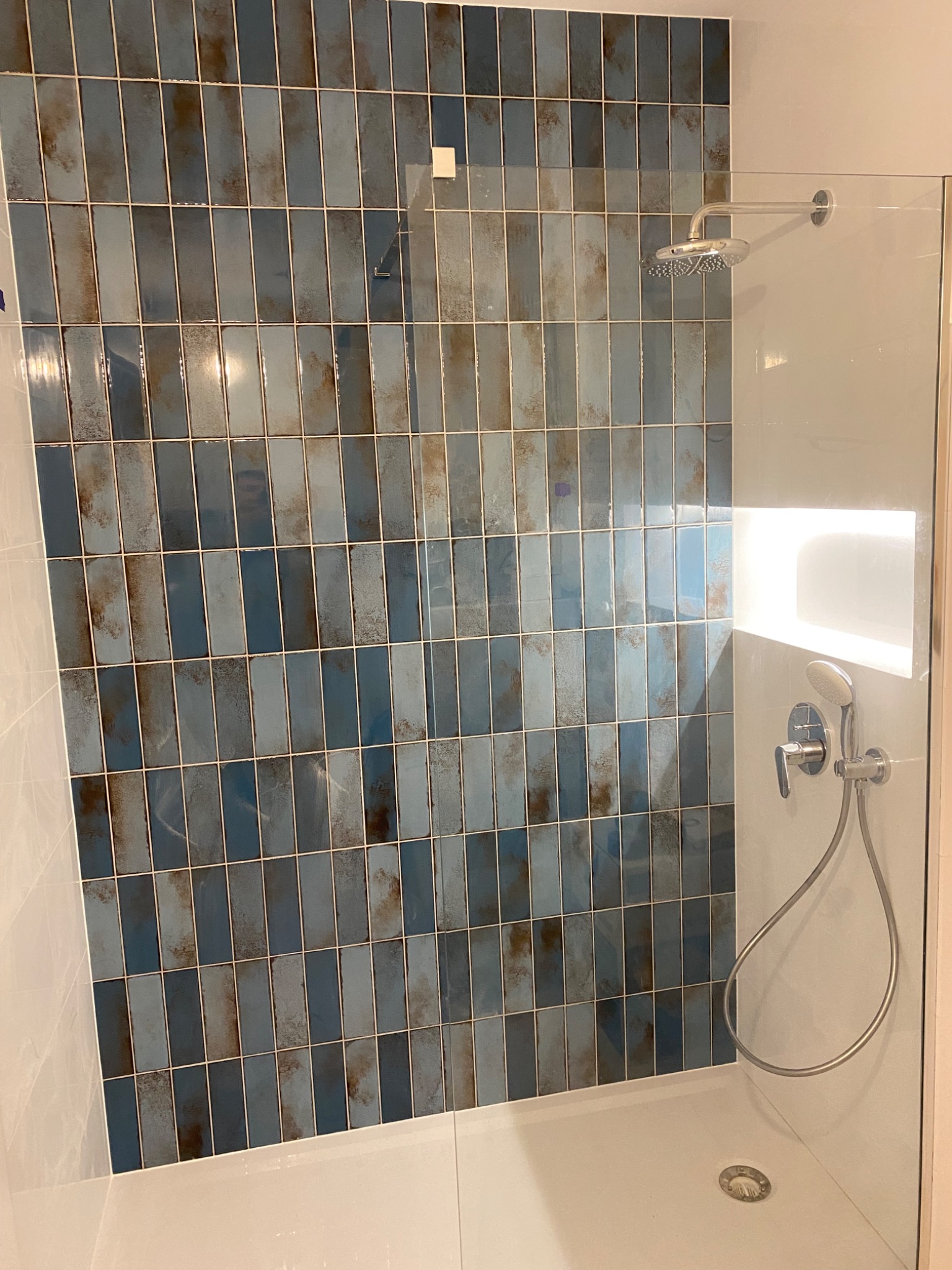 Wykończona kabina prysznicowa z niebiesko-brązowymi, pionowo ułożonymi płytkami imitującymi cegłę, chromowaną armaturą i wnęką z podświetleniem LED.