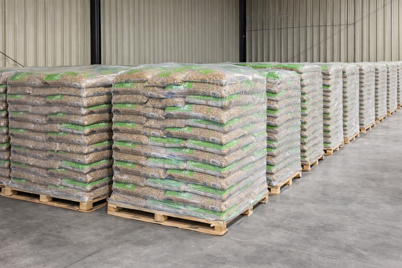 Rząd palet z workami pelletu, zabezpieczonych folią, w magazynie oświetlonym światłem dziennym. Widok z perspektywy podłogi, ukazujący regularny układ.