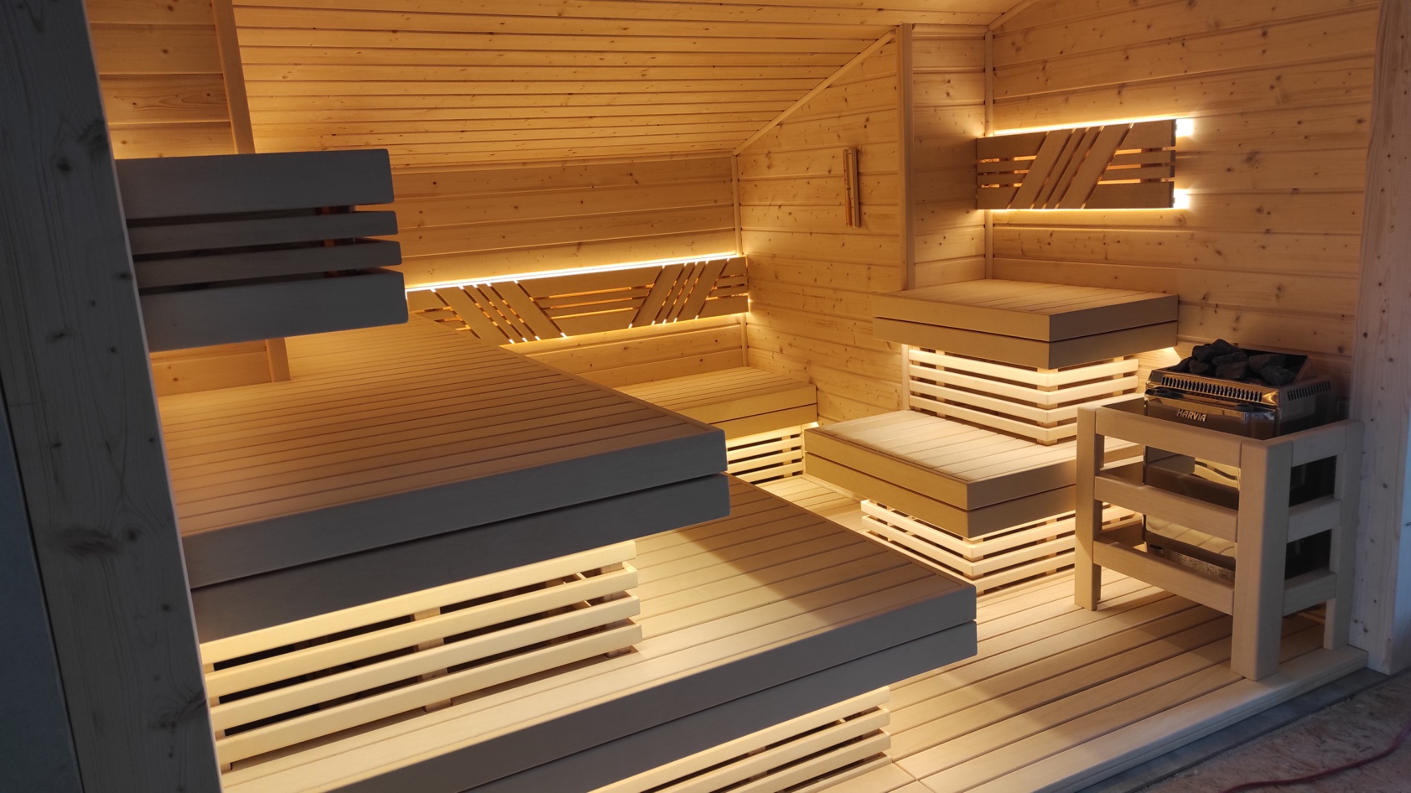 Wnętrze drewnianej kabiny z podświetlanymi ławkami i piecem Harvia z kamieniami.