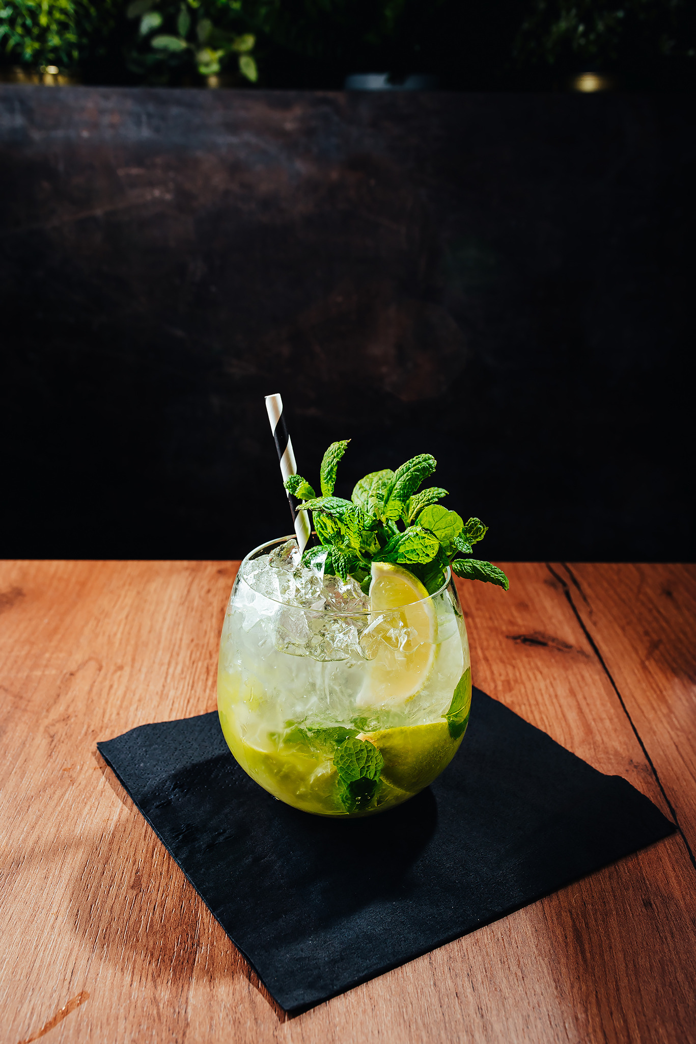 Orzeźwiający koktajl mojito z kruszonym lodem, miętą i limonką w szklance na czarnej podkładce, sfotografowany w Topola Mała na drewnianym stole z ciemnym tłem.