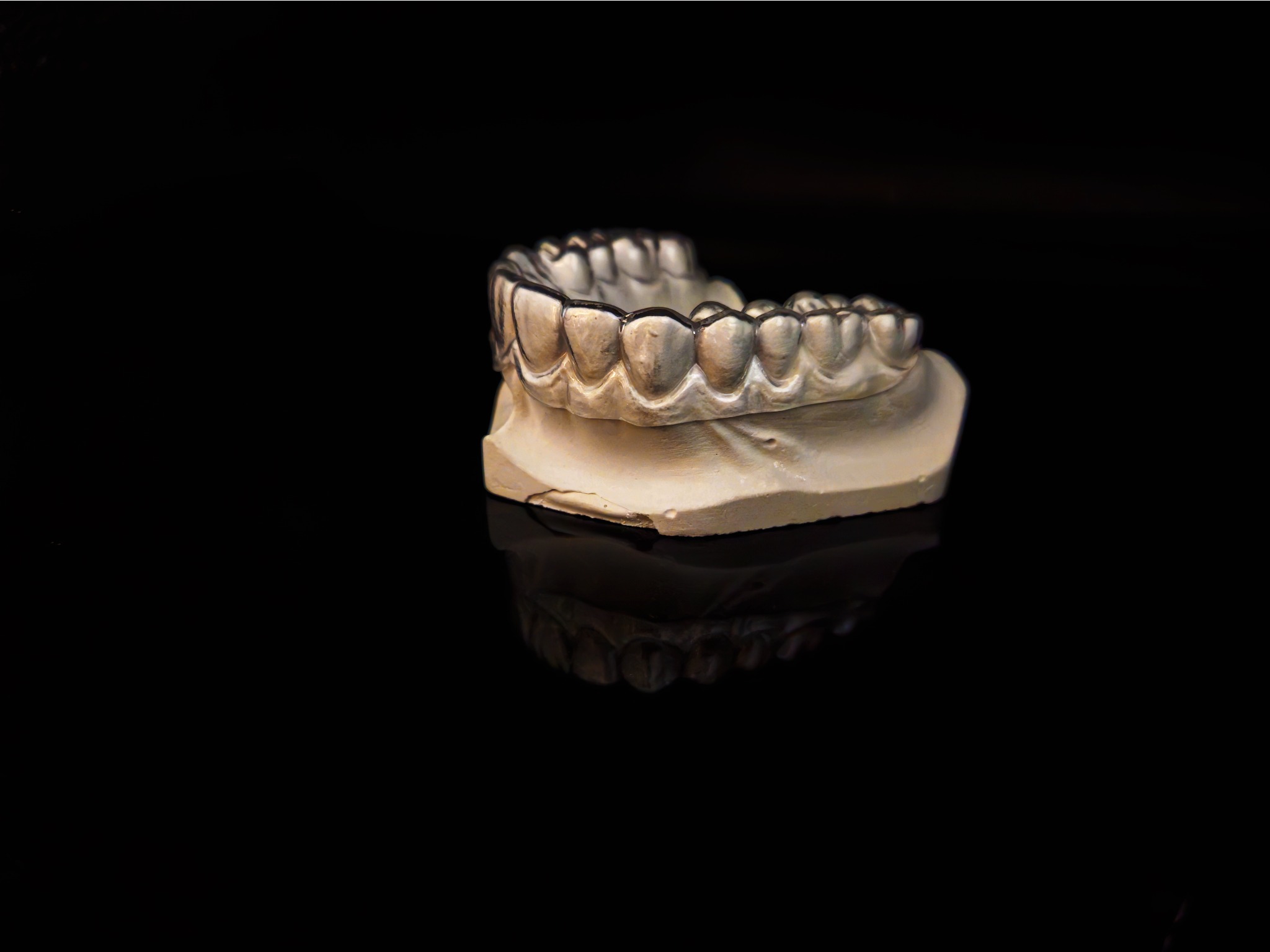 Gipsowy model szczęki z założonym przezroczystym aparatem ortodontycznym na czarnym, błyszczącym tle.