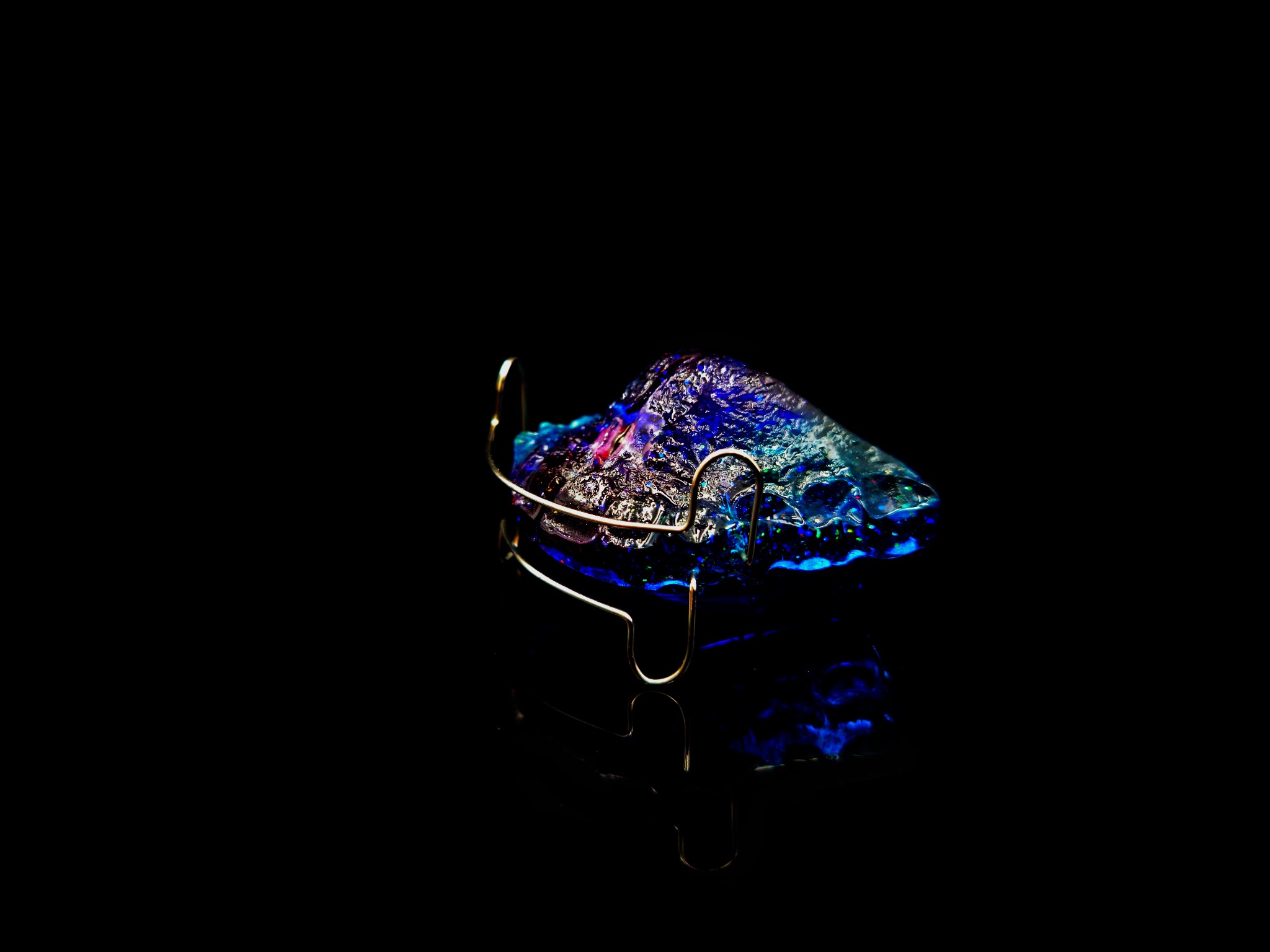 Aparat ortodontyczny ruchomy, wykonany z niebieskiego akrylu z metalowymi elementami mocującymi, leżący na czarnym, błyszczącym tle.