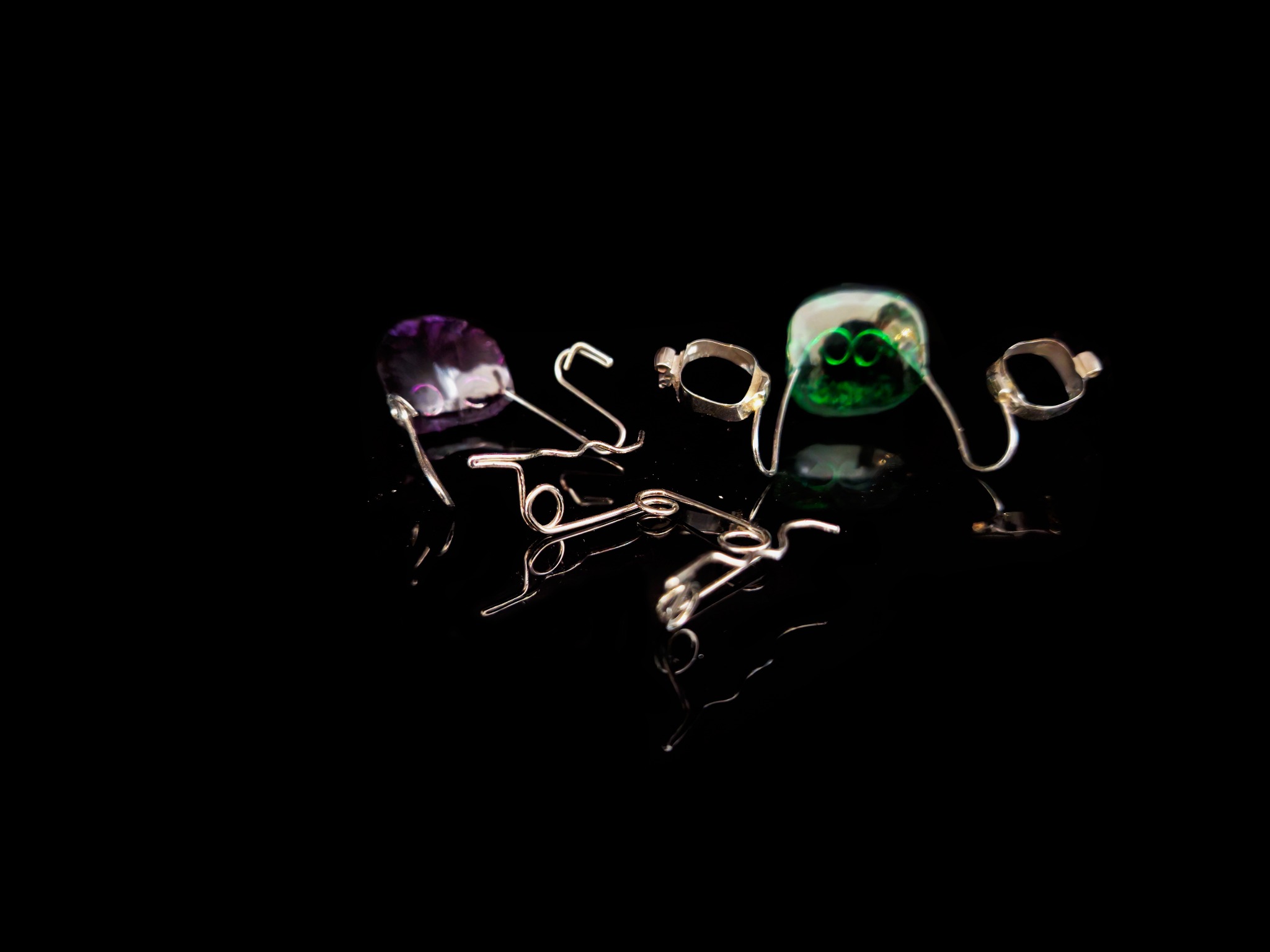 Aparat ortodontyczny z kolorowymi elementami akrylowymi (fioletowy i zielony) oraz metalowymi klamrami, ułożony na czarnej, błyszczącej powierzchni, tworzącej lustrzane odbicie.