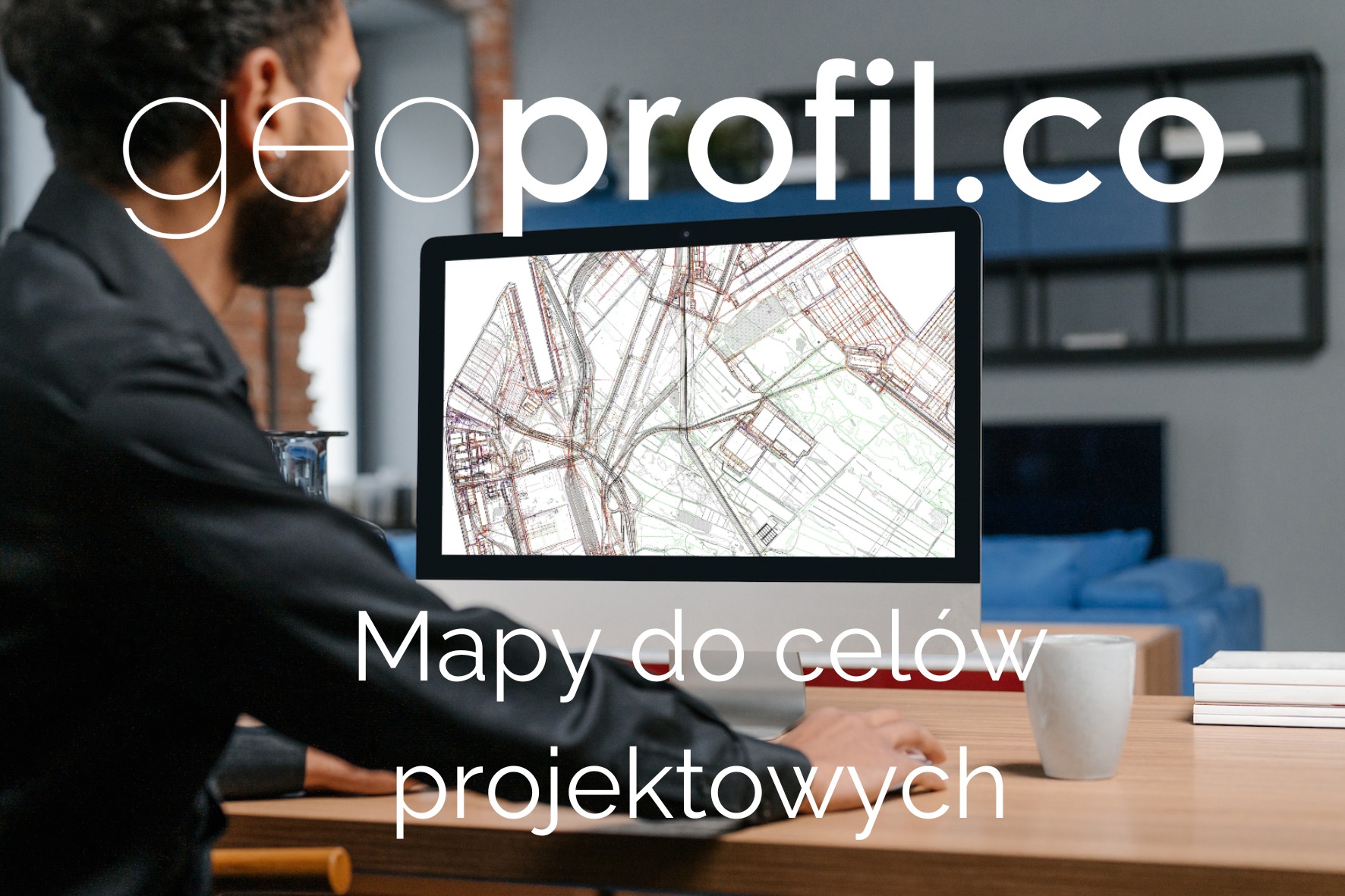 Mężczyzna w czarnej marynarce siedzi przed monitorem, na którym wyświetlona jest mapa do celów projektowych; na biurku stoi kubek i leżą książki.