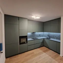 Nowoczesna kuchnia w odcieniach zieleni z matowymi frontami, czarnymi detalami i marmurowym backsplashiem podświetlonym LED, widziana pod kątem z parkietem w jodełkę na pierwszym planie.