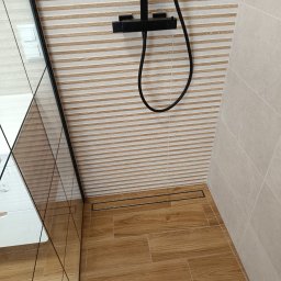 Bud Rud - Nowoczesna kabina prysznicowa z drewnopodobnymi płytkami na podłodze i ścianie, czarna armatura, szklana ścianka. Minimalistyczny design z odpływem liniowym.