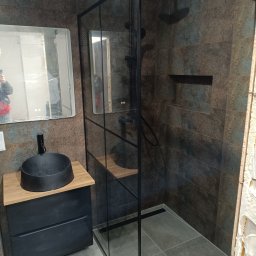 Bud Rud - Nowoczesna łazienka z kabiną prysznicową typu walk-in, czarną armaturą i umywalką nablatową. Widoczne płytki imitujące kamień i lustro z podświetleniem LED.