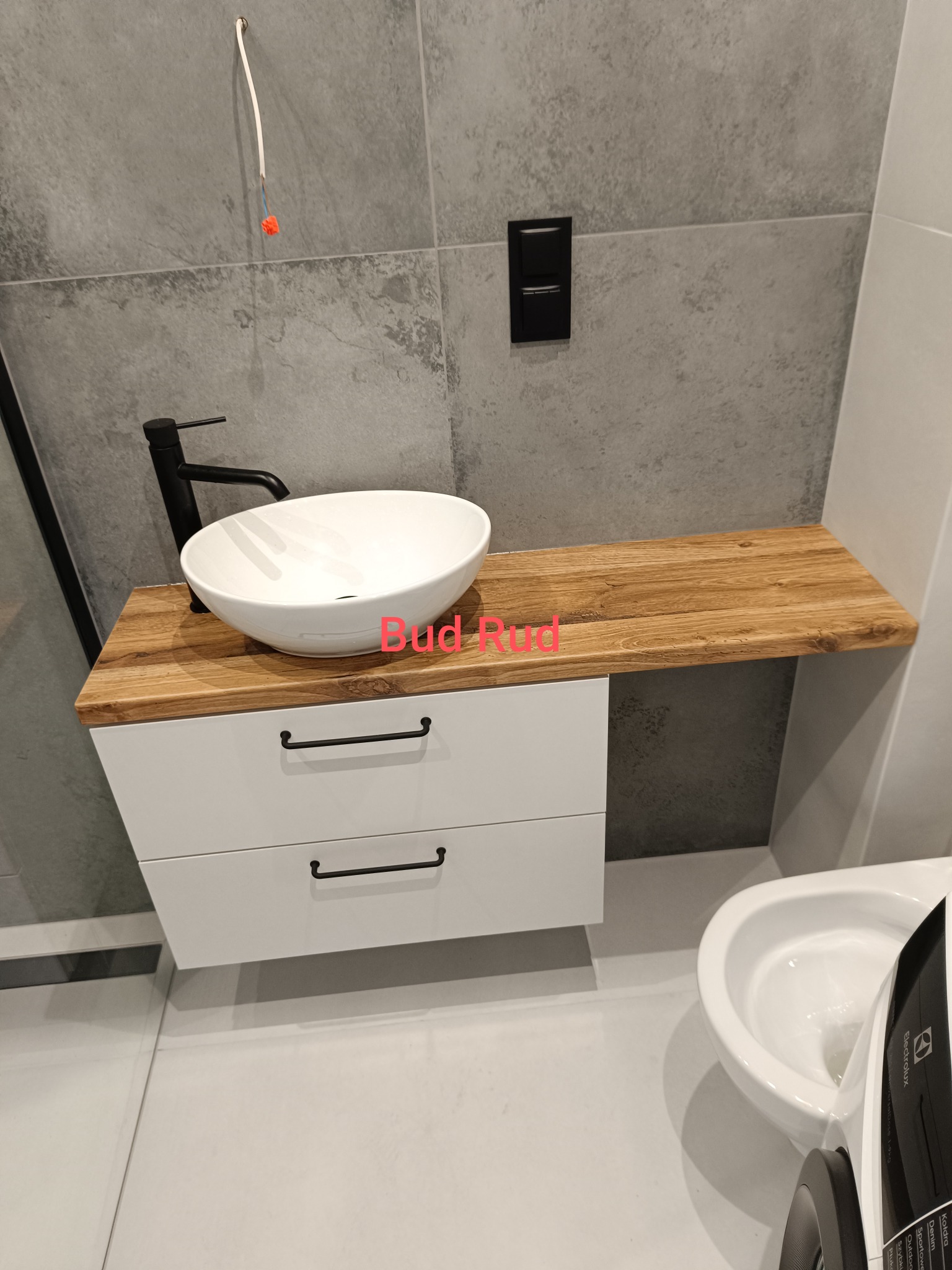 Nowoczesna łazienka we Wrocławiu: biała umywalka nablatowa na drewnianym blacie, minimalistyczna szafka z czarnymi uchwytami, szare płytki i czarna bateria.