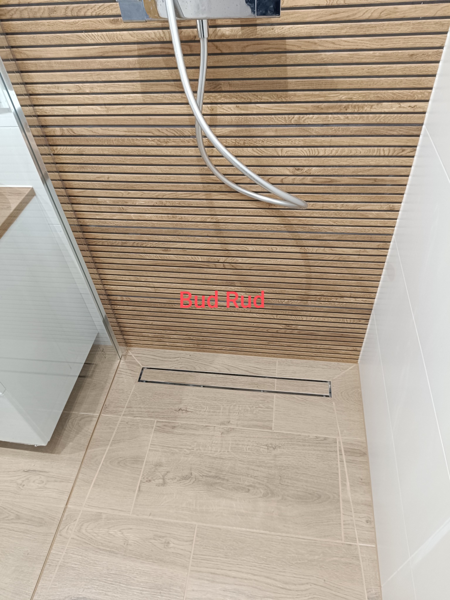 Nowoczesna kabina prysznicowa z drewnopodobną okładziną ścienną i odpływem liniowym. Jasne płytki podłogowe imitujące drewno. Minimalistyczny design.