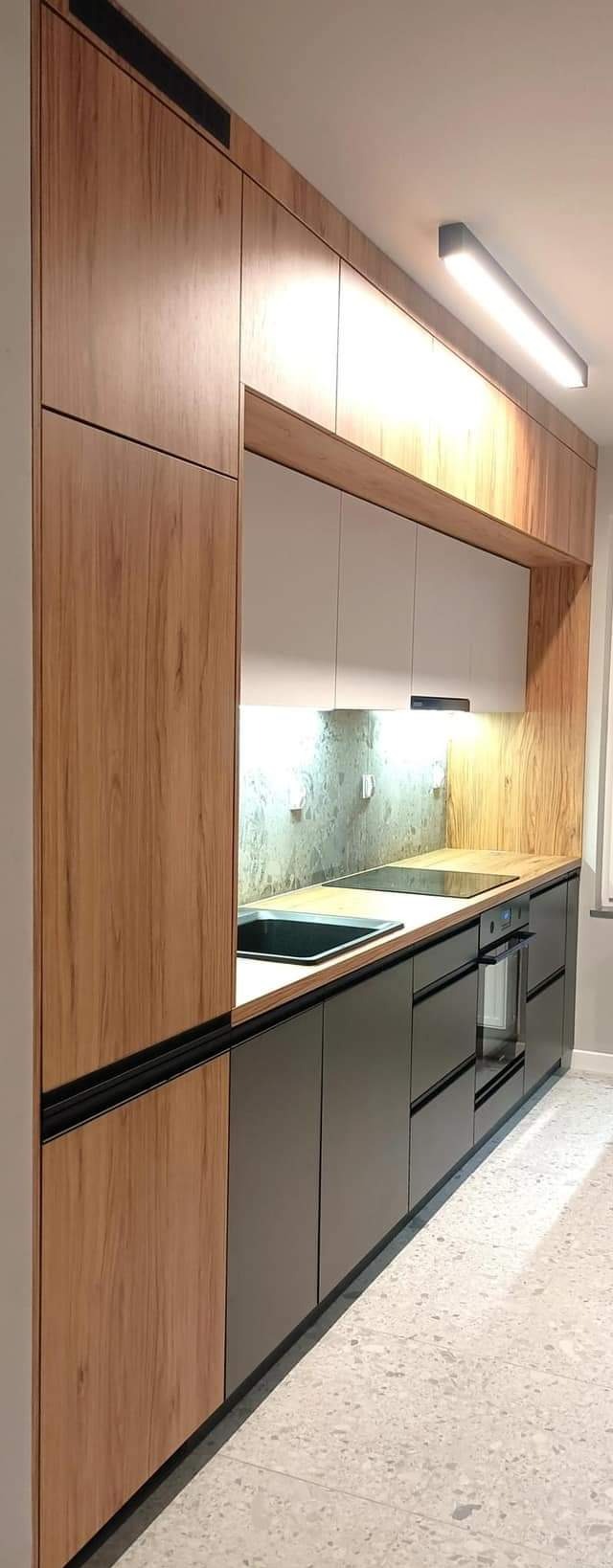 Nowoczesna kuchnia z drewnianymi i szarymi szafkami, czarnym zlewem i blatem. Oświetlenie LED podkreśla minimalistyczny design i fakturę materiałów.