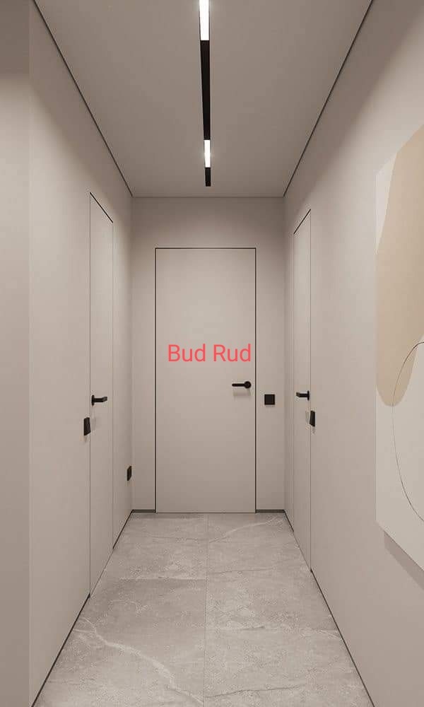 Minimalistyczny korytarz z trzema białymi drzwiami z czarnymi klamkami, szarą podłogą z płytek i nowoczesnym oświetleniem sufitowym. Neutralna kolorystyka.