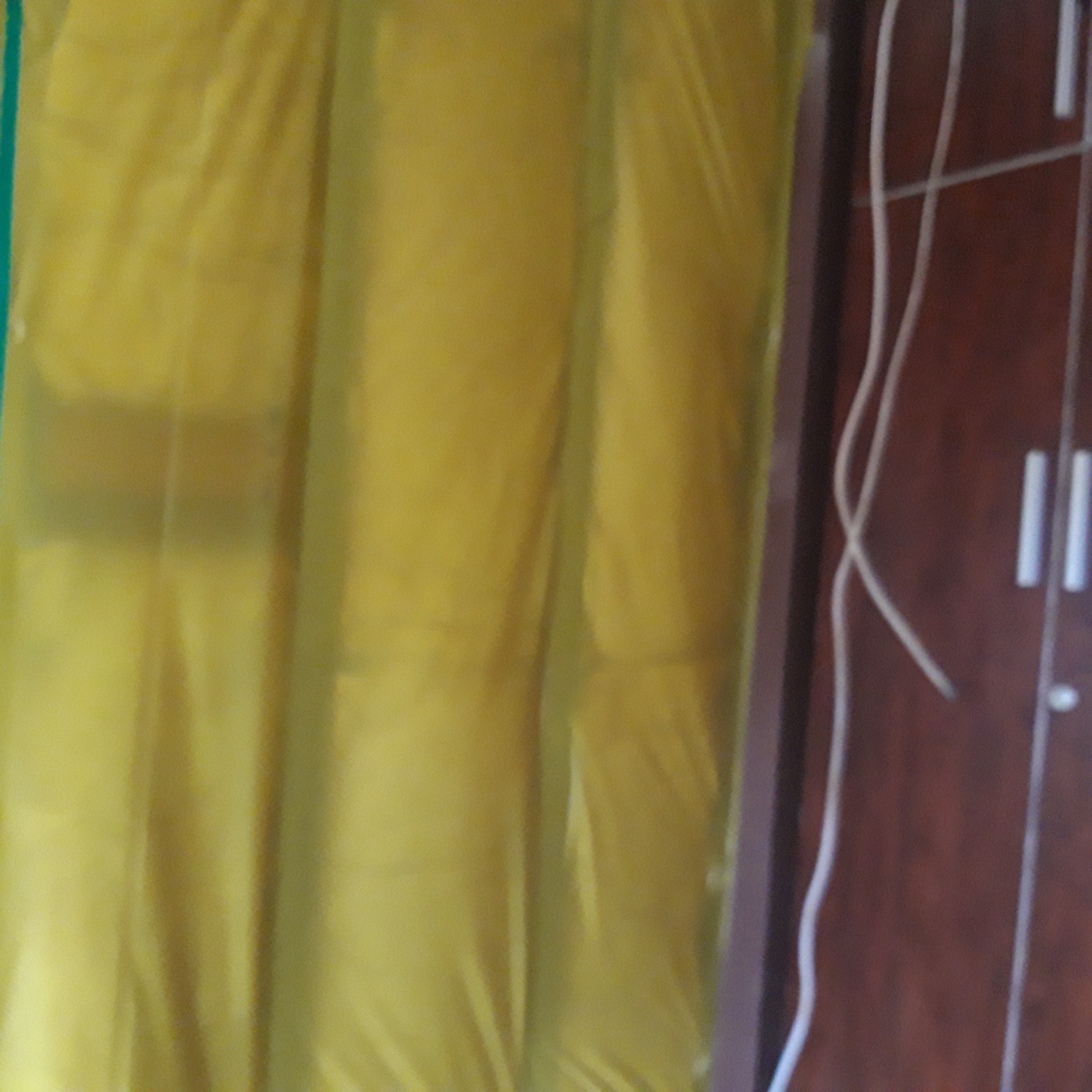 Folia ochronna w kolorze żółtym, zabezpieczająca ścianę podczas prac malarskich, widoczny fragment szafy w tle.