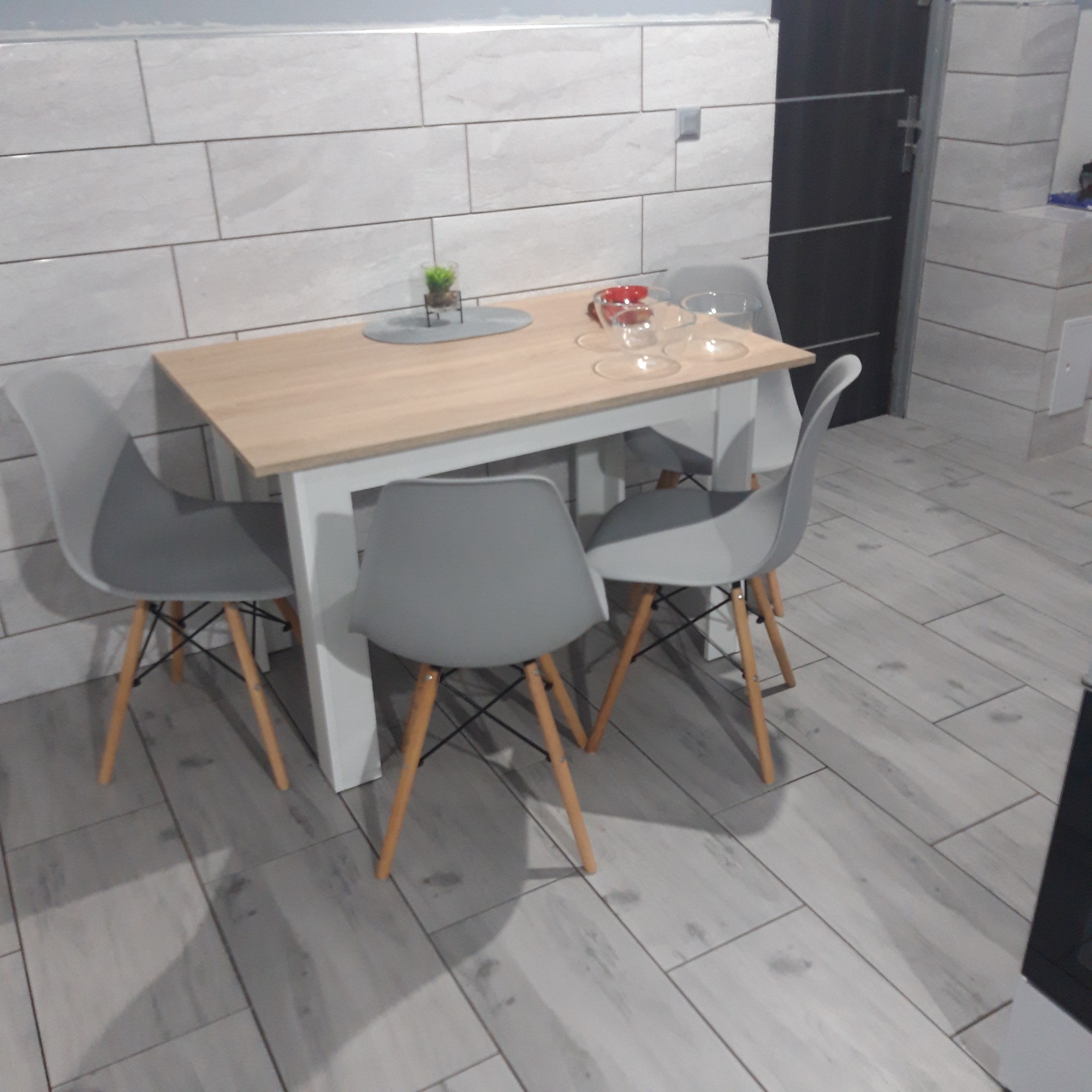 Jasna kuchnia w Myśliborzu z płytkami imitującymi drewno na podłodze i ścianach, stół z czterema szarymi krzesłami.