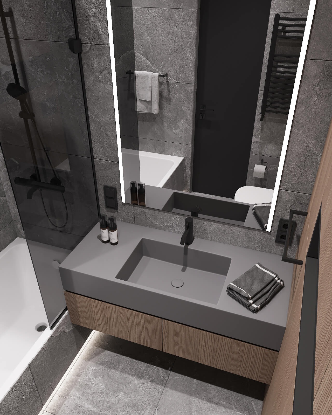 Nowoczesna łazienka z szarą umywalką nablatową, drewnianą szafką pod umywalką, podświetlanym lustrem i szarą płytką imitującą kamień na ścianach. Widoczna kabina prysznicowa ze szklanymi drzwiami...