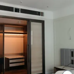 Nowoczesna szafa wnękowa z przesuwnymi drzwiami z widocznym oświetleniem wewnętrznym i wbudowanymi szufladami, w tle ściana z obrazami i wezgłowiem łóżka.