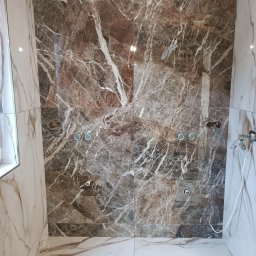 Firma Remont-Budowlana RS-BUD - Wykończona kabina prysznicowa z brązowymi i białymi płytkami imitującymi marmur, widoczne przygotowane punkty instalacyjne. Estetyczne połączenie kolorów i wzorów.