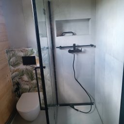 Firma Remont-Budowlana RS-BUD - Nowoczesna łazienka z kabiną prysznicową typu walk-in, czarną armaturą i płytkami w tropikalne wzory. Widoczna toaleta i wnęka w ścianie. Minimalistyczny design.