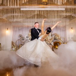 PHU KAR-EVENTS - Para młoda w tańcu w chmurze dymu na sali weselnej z dekoracjami w stylu boho i kryształowym żyrandolem.